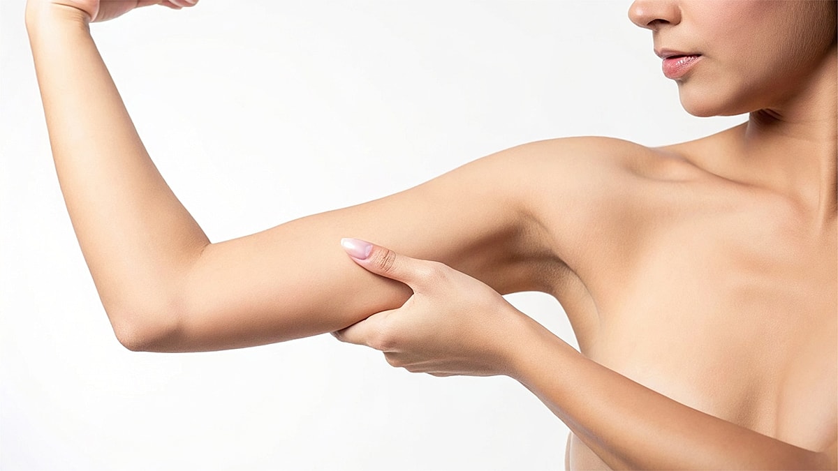 What Is a Scarless Arm Lift and Who Is the Best Candidate - Woman flexing her arm muscle in soft lighting