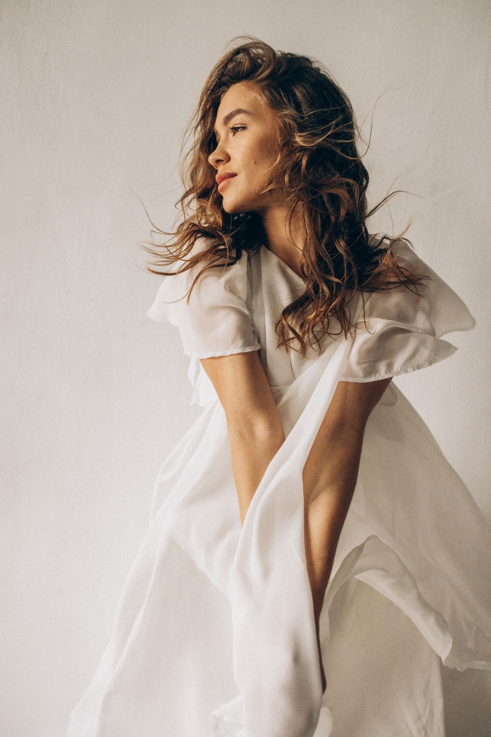 Woman in flowing white dress against light background