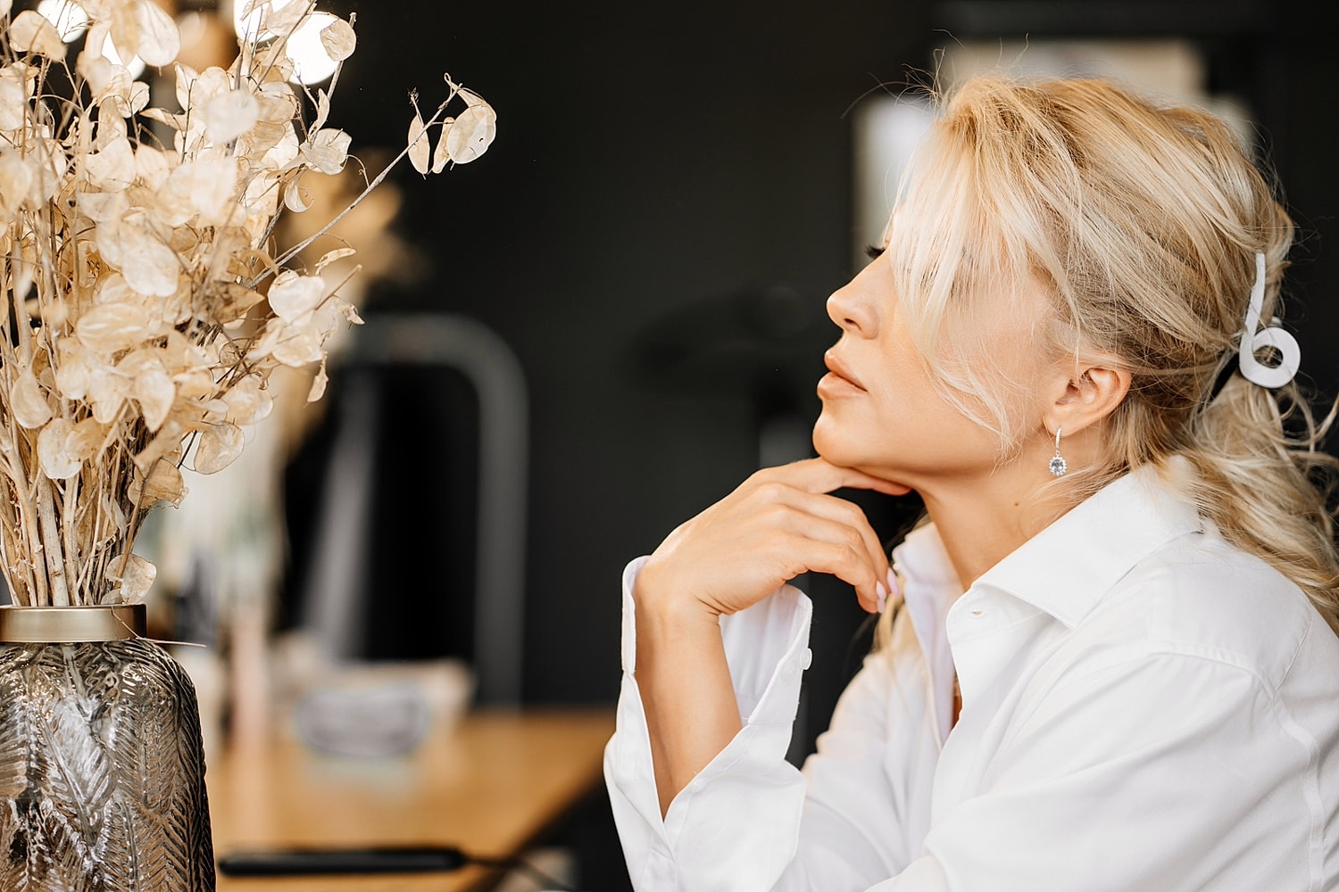 Woman in white shirt contemplating with dried flowers.