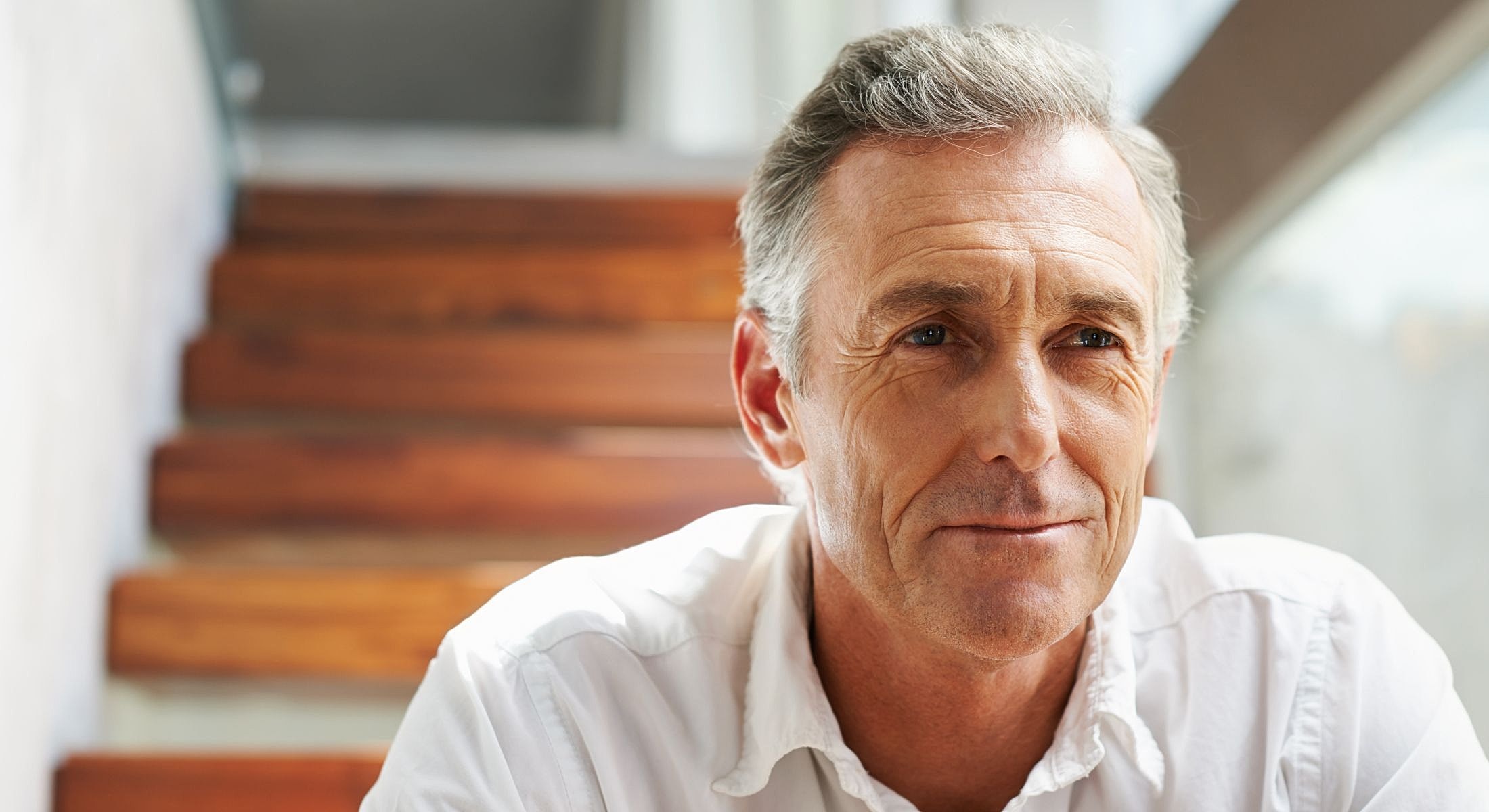 Houston plastic surgery for men model smiling man sitting on wooden stairs.