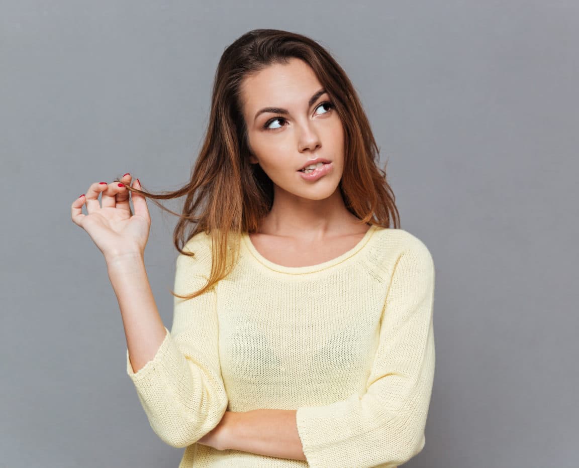 Young pensive woman in sweater looking away and biting lips